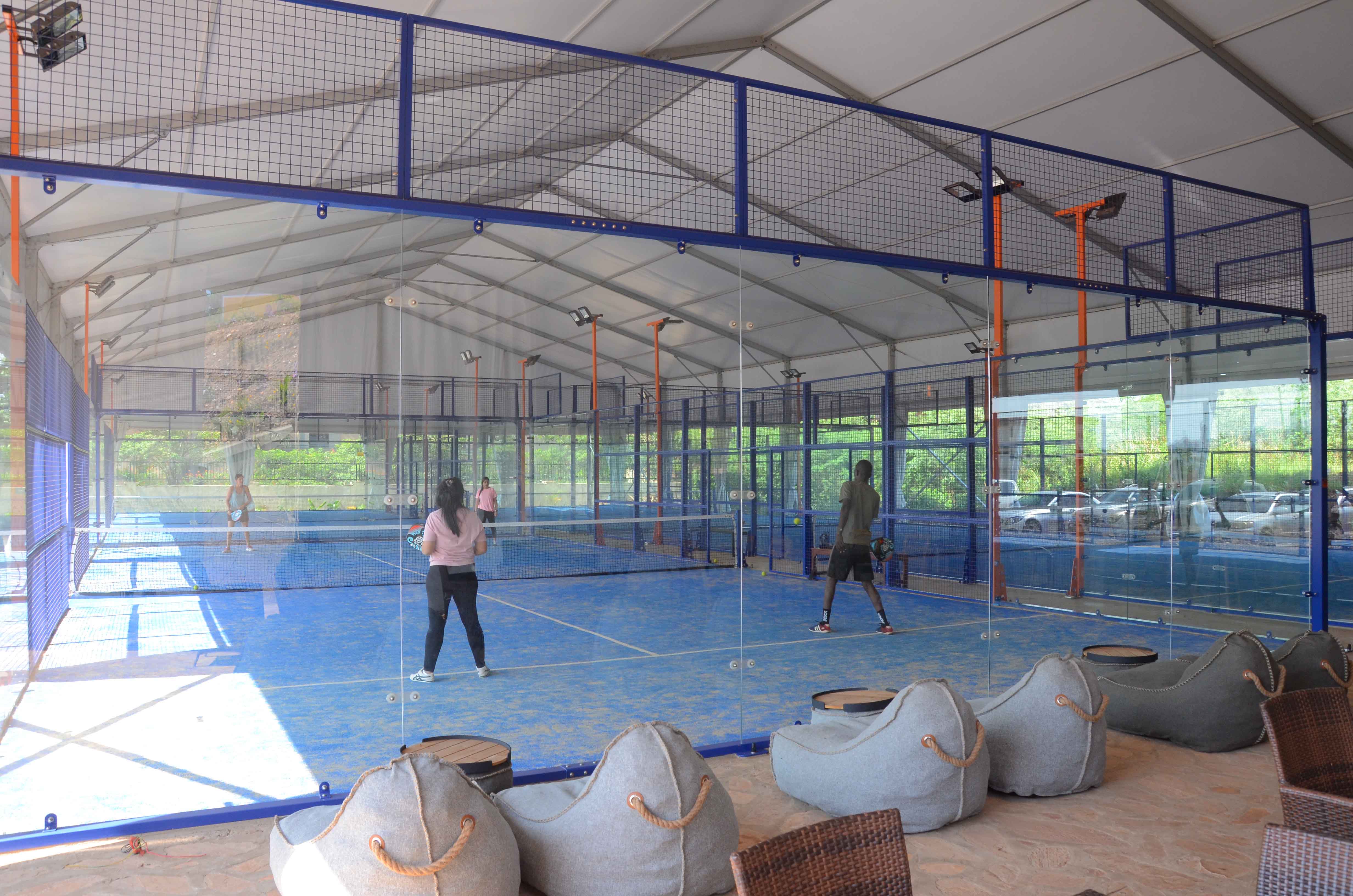 Two players in active play on a blue indoor padel court with glass back wall