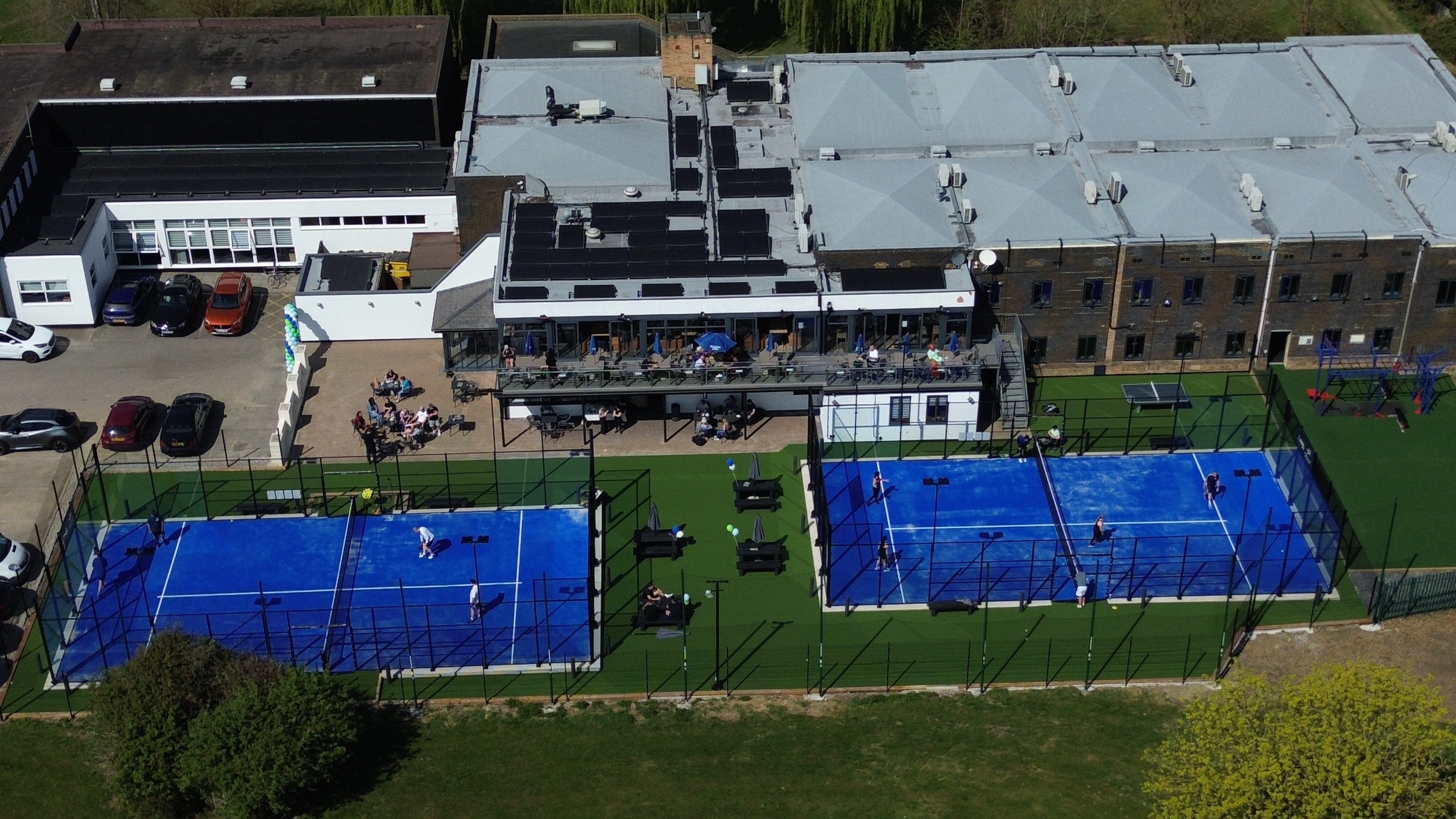 Aerial view of padel courts with glass walls and players mid-game