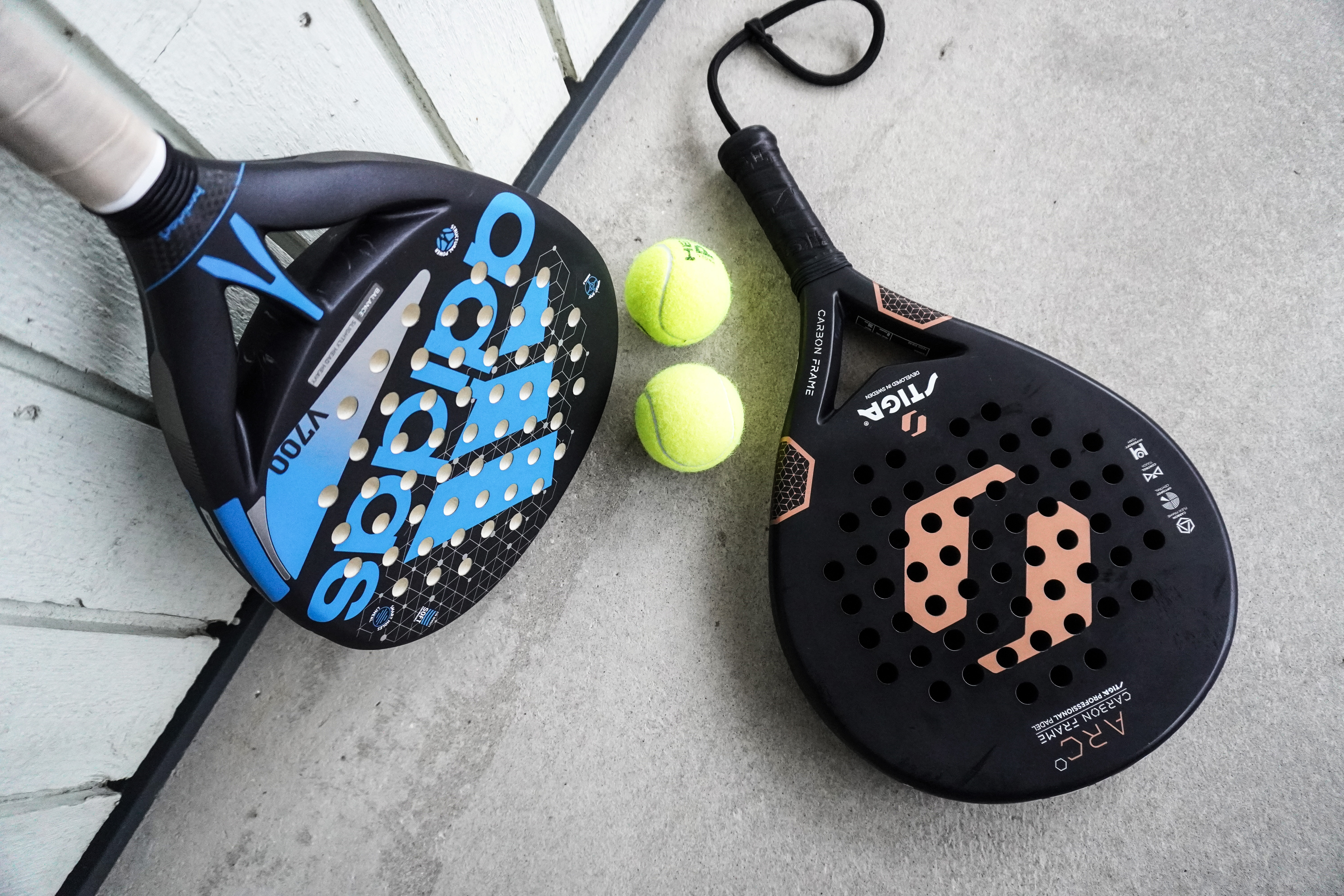 Two padel rackets with perforated faces and yellow padel balls — the solid racket is what sets padel apart from tennis